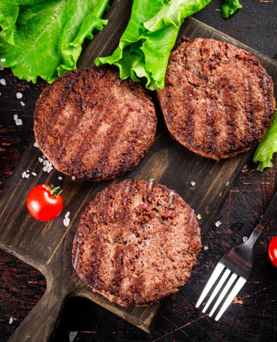 Burger grill on a cutting board with tomatoes and greens.