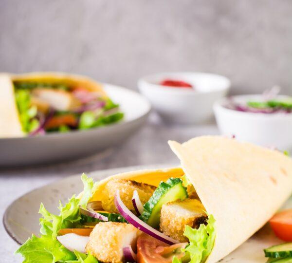 Tortilla wrap with cucumber, chicken and tomato on a plate. Mexican cuisine. Vertical view